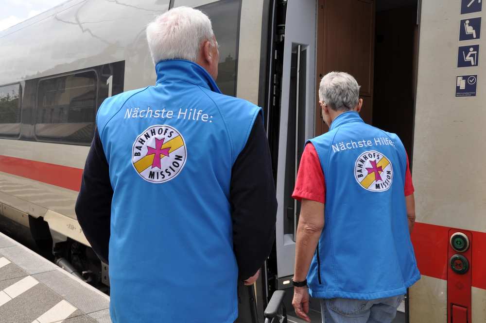 Zwei Mitarbeiter der Bahnhofsmission stehen am Bahngleis.